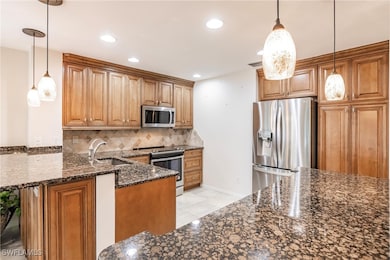 Kitchen featuring stainless steel appliances, hanging light fixtures, sink, and dark stone counters