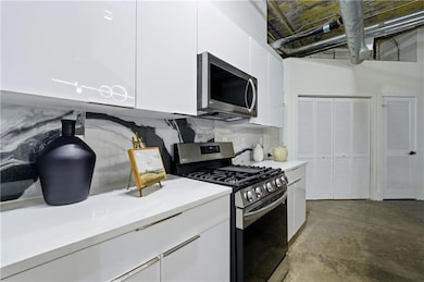 Kitchen with appliances with stainless steel finishes, white cabinets, unfinished concrete floors, modern cabinets, and backsplash
