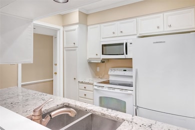 Kitchen with white appliances, white cabinetry, light stone countertops, and crown molding
