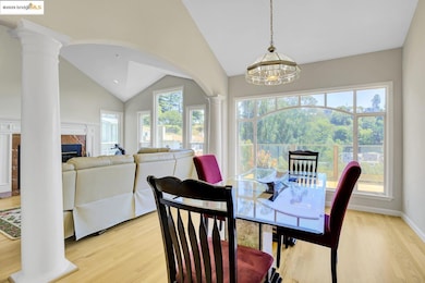 Dining area featuring decorative columns, light wood-style flooring, a chandelier, a fireplace, and vaulted ceiling