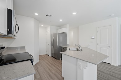 Kitchen with light stone counters, appliances with stainless steel finishes, a peninsula, light wood-type flooring, and recessed lighting