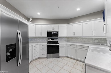 Kitchen featuring appliances with stainless steel finishes, white cabinets, decorative backsplash, light tile patterned floors, and recessed lighting