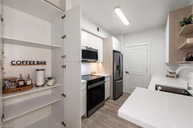 Kitchen with open shelves, stainless steel appliances, light wood-style flooring, white cabinets, and light stone countertops