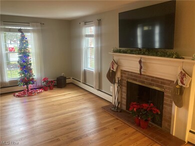 Living room featuring a brick fireplace, baseboard heating, and hardwood flooring.