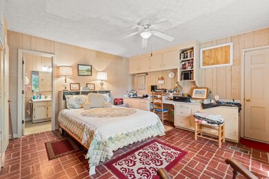 Bedroom with brick flooring, wooden walls, an office area, a ceiling fan, and ensuite bath
