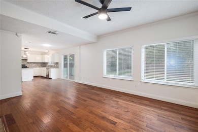 Unfurnished living room featuring dark wood-style floors, a textured ceiling, ornamental molding, and ceiling fan