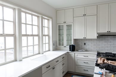 Kitchen featuring white cabinetry, tasteful backsplash, stainless steel gas range oven, glass insert cabinets, and light stone counters