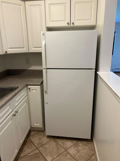 Kitchen featuring white cabinets, freestanding refrigerator, dark countertops, and a baseboard heating unit
