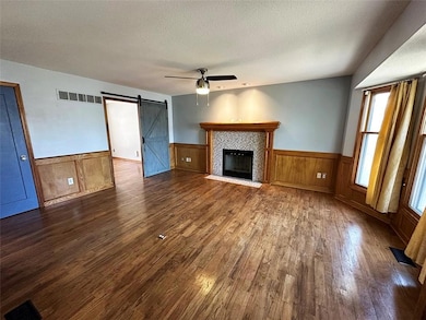 Unfurnished living room featuring a barn door, dark wood finished floors, a textured ceiling, a wainscoted wall, and a tiled fireplace