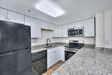 Kitchen featuring black appliances, light stone countertops, and white cabinetry