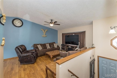 Living room with wood finished floors, a ceiling fan, a textured ceiling, and lofted ceiling