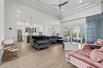 Living area featuring light wood-type flooring, a tray ceiling, recessed lighting, a high ceiling, and a ceiling fan