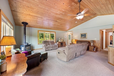 Living room featuring wood ceiling, carpet floors, a wood stove, lofted ceiling, and a ceiling fan