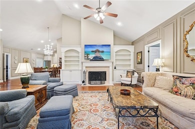 Living area featuring high vaulted ceiling, a decorative wall, wood finished floors, built in features, and a fireplace with flush hearth