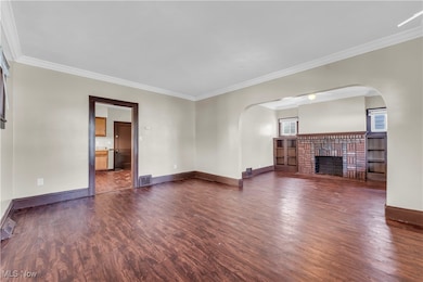 Unfurnished living room featuring arched walkways, ornamental molding, dark wood-type flooring, and a brick fireplace