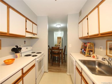 Kitchen featuring white appliances, white cabinetry, light countertops, and brown cabinets