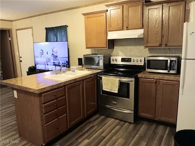 Kitchen with stainless steel appliances, a peninsula, dark wood-type flooring, brown cabinets, and under cabinet range hood