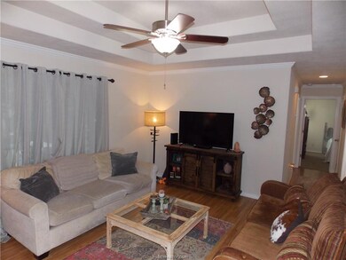 Living room with hardwood / wood-style flooring, ceiling fan, a raised ceiling, and crown molding