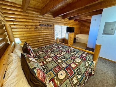 Bedroom featuring carpet, log walls, electric panel, a wood ceiling with exposed beams, and a textured wall
