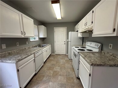 Kitchen featuring white appliances, white cabinets, under cabinet range hood, stone finish floors, and light stone countertops