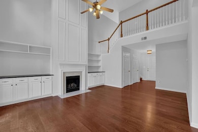 Unfurnished living room with a towering ceiling, a ceiling fan, wood finished floors, and a fireplace