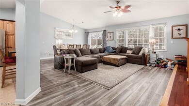 Living room featuring ceiling fan with notable chandelier, light hardwood / wood-style flooring, and lofted ceiling