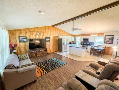 Living room featuring a chandelier, wooden walls, light wood-type flooring, a textured ceiling, and ceiling fan
