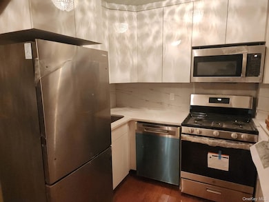 Kitchen featuring stainless steel appliances, dark wood-style floors, decorative backsplash, white cabinetry, and light stone counters