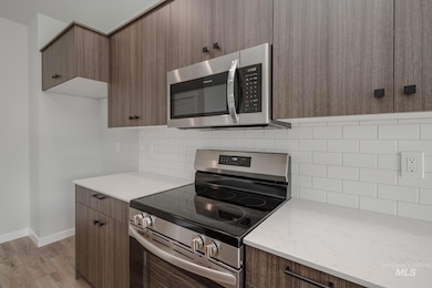 Kitchen featuring appliances with stainless steel finishes, backsplash, modern cabinets, light wood-style floors, and light stone countertops