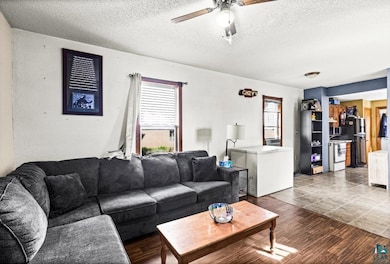 Living room with a textured ceiling, a ceiling fan, and wood finished floors