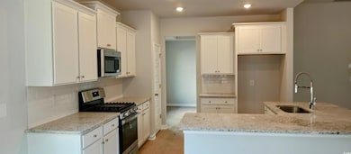 Kitchen with white cabinetry, appliances with stai