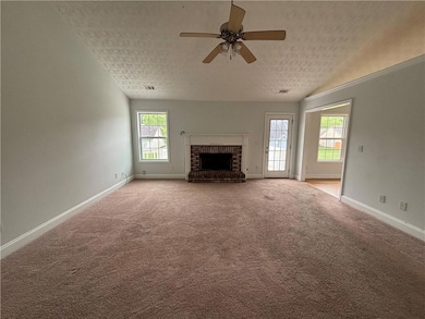 Unfurnished living room with a textured ceiling, a fireplace, ceiling fan, baseboards, and light colored carpet