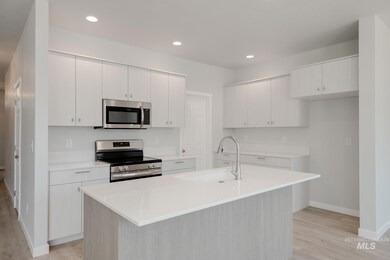 Kitchen with stainless steel appliances, light wood finished floors, light countertops, white cabinetry, and a center island with sink