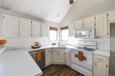Kitchen featuring white appliances, lofted ceiling, light countertops, decorative backsplash, and dark wood-type flooring