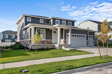 View of front of house with stone siding, a front yard, concrete driveway, a garage, and a porch