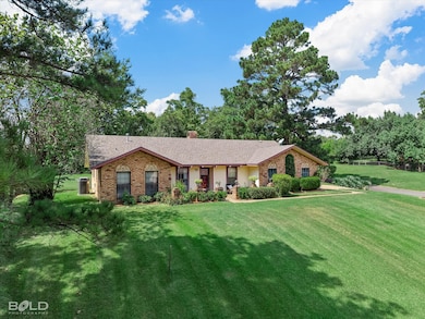 Ranch-style house featuring a chimney, a front yard, brick siding, roof with shingles, and a porch