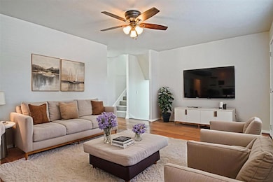 Living room featuring wood finished floors, ceiling fan, and stairway