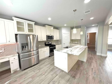 Kitchen featuring backsplash, stainless steel appliances, light stone counters, glass insert cabinets, and white cabinets