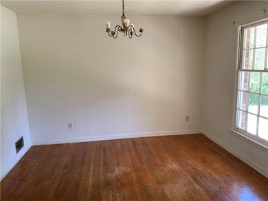 Empty room featuring hardwood / wood-style floors, a chandelier, healthy amount of natural light, and baseboards