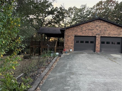 View of property exterior featuring driveway, brick siding, an attached garage, and a wooden deck
