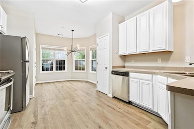 Kitchen featuring stainless steel appliances, a chandelier, light wood finished floors, white cabinets, and pendant lighting