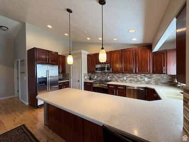 Kitchen with stainless steel appliances, a peninsula, a textured ceiling, light countertops, and tasteful backsplash