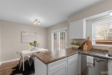 Kitchen with a peninsula, dishwasher, dark countertops, white cabinetry, and dark wood-style flooring