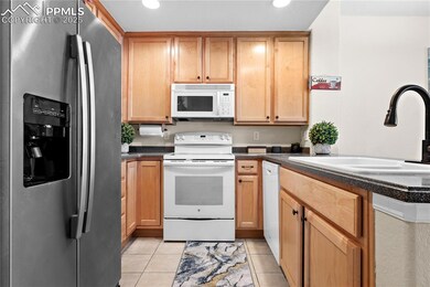 Kitchen featuring white appliances, dark countertops, light tile patterned floors, and recessed lighting