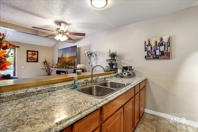 Kitchen with brown cabinetry, a ceiling fan, a textured ceiling, a peninsula, and light tile patterned floors