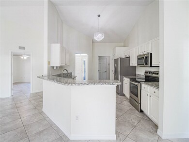 Kitchen with stainless steel appliances, high vaulted ceiling, white cabinetry, a chandelier, and light tile patterned floors