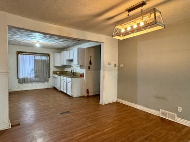 Kitchen featuring a textured ceiling, white cabinets, dark countertops, dark wood finished floors, and decorative light fixtures