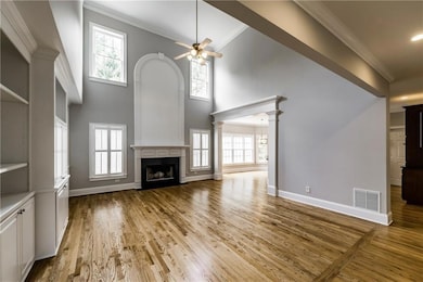 Unfurnished living room with a ceiling fan, a fireplace with flush hearth, crown molding, light wood finished floors, and a high ceiling