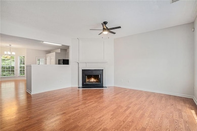 Unfurnished living room featuring a high end fireplace, light wood finished floors, a textured ceiling, a chandelier, and a ceiling fan