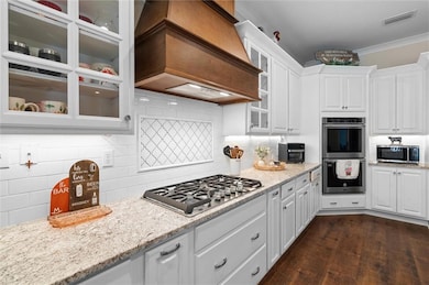 Kitchen with wall chimney exhaust hood, stainless steel appliances, white cabinets, and crown molding
